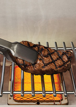 steak held by tongs over grill surface 
